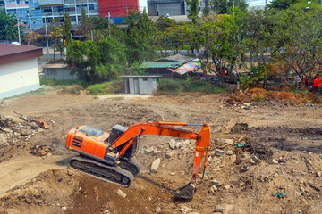 Wall Mural - Excavator at work on construction site, thickets and other old houses around