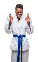 Wall Mural - Young african american man over isolated background wearing kimono smiling crossing fingers with hope and eyes closed. Luck and superstitious concept.