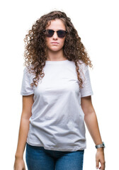 Wall Mural - Beautiful brunette curly hair young girl wearing sunglasses over isolated background with serious expression on face. Simple and natural looking at the camera.