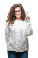 Canvas Print - Beautiful brunette curly hair young girl wearing winter sweater over isolated background showing and pointing up with finger number one while smiling confident and happy.