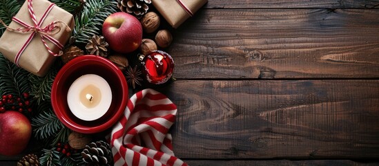 Poster - An arrangement of Christmas items including a red bowl filled with pine cones a gift box in kraft paper pine branches a candle nuts anise apples and a red and white striped winter scarf on a dark woo