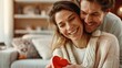 © Pinklife - A couple embracing with special care, focusing on a red heart-shaped object, highlighting their mutual love and tenderness in an intimate indoor setting full of warmth.