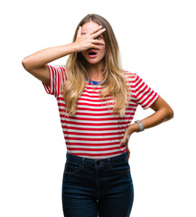 Canvas Print - Young beautiful blonde woman over isolated background peeking in shock covering face and eyes with hand, looking through fingers with embarrassed expression.