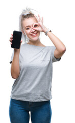 Canvas Print - Young blonde woman showing screen of smartphone over isolated background with happy face smiling doing ok sign with hand on eye looking through fingers