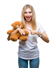 Poster - Young beautiful blonde woman holding teddy bear over isolated background very happy pointing with hand and finger