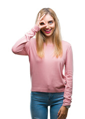 Canvas Print - Young beautiful blonde woman wearing pink winter sweater over isolated background doing ok gesture with hand smiling, eye looking through fingers with happy face.