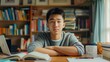 © gn8 - Focused Chinese Male Student in Casual Attire Studying at a Desk, Surrounded by Books and a Laptop in a Library Setting