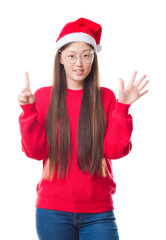 Wall Mural - Young Chinese woman over isolated background wearing christmas hat showing and pointing up with fingers number six while smiling confident and happy.