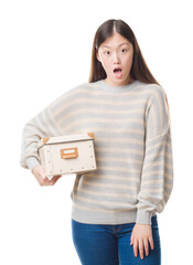 Wall Mural - Young Chinese woman over isolated background holding a box scared in shock with a surprise face, afraid and excited with fear expression