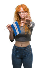 Sticker - Young redhead woman holding flag of Argentina with open hand doing stop sign with serious and confident expression, defense gesture