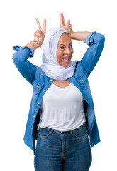 Poster - Middle age eastern arab woman wearing arabian hijab over isolated background Posing funny and crazy with fingers on head as bunny ears, smiling cheerful