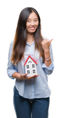 Sticker - Young asian woman real state agent holding house isolated background pointing and showing with thumb up to the side with happy face smiling