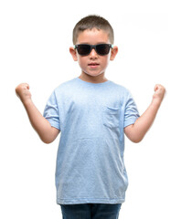 Wall Mural - Dark haired little child wearing sunglasses screaming proud and celebrating victory and success very excited, cheering emotion