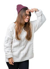 Poster - Young beautiful brunette hipster woman wearing glasses and winter hat over isolated background very happy and smiling looking far away with hand over head. Searching concept.