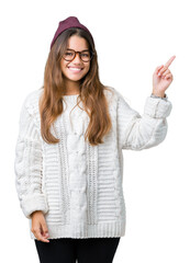 Sticker - Young beautiful brunette hipster woman wearing glasses and winter hat over isolated background with a big smile on face, pointing with hand and finger to the side looking at the camera.