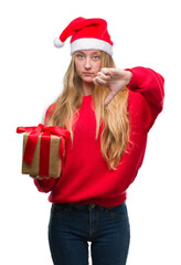 Poster - Blonde teenager woman wearing santa claus hat with angry face, negative sign showing dislike with thumbs down, rejection concept