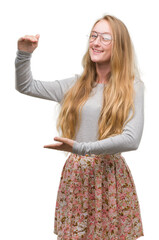 Canvas Print - Blonde teenager woman wearing flowers skirt gesturing with hands showing big and large size sign, measure symbol. Smiling looking at the camera. Measuring concept.