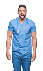 Wall Mural - Handsome young doctor surgeon man over isolated background sticking tongue out happy with funny expression. Emotion concept.