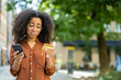 © Tetiana - Upset young African American woman standing outside on the street, holding a cell phone and looking worriedly at a credit card
