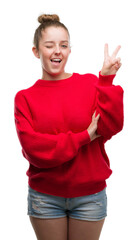 Wall Mural - Young blonde woman wearing bun and red sweater smiling with happy face winking at the camera doing victory sign. Number two.