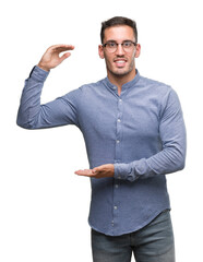 Canvas Print - Handsome young elegant man wearing glasses gesturing with hands showing big and large size sign, measure symbol. Smiling looking at the camera. Measuring concept.