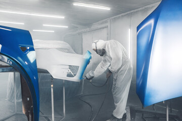 Wall Mural - Car paint worker spraying blue paint to car body element using spray gun in vehicle workshop chamber. Complex restoration of automobile body. 