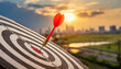 © netsay - Close up red dart arrow hitting target center dartboard on sunset background. Business targeting and focus concept.