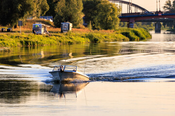 A small motor boat floats along the river against the backdrop of a city bridge. Warm sunset light.