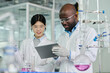 © pressmaster - Two young intercultural chemists looking at screen of tablet held by African American male scientist while carrying out new trial