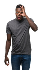 Poster - Young african american man wearing grey t-shirt doing ok gesture shocked with surprised face, eye looking through fingers. Unbelieving expression.