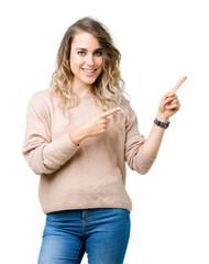 Wall Mural - Beautiful young blonde woman wearing sweatershirt over isolated background smiling and looking at the camera pointing with two hands and fingers to the side.