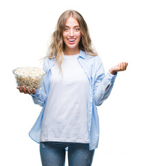 Poster - Beautiful young blonde woman eating popcorn over isolated background screaming proud and celebrating victory and success very excited, cheering emotion