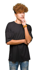 Wall Mural - Young handsome man with afro hair wearing black t-shirt with hand on chin thinking about question, pensive expression. Smiling with thoughtful face. Doubt concept.