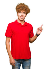 Wall Mural - Young handsome man with afro hair wearing red t-shirt with a big smile on face, pointing with hand and finger to the side looking at the camera.