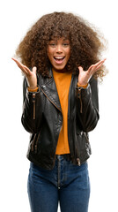 Wall Mural - African american woman wearing a leather jacket very happy and excited, winner expression celebrating victory screaming with big smile and raised hands