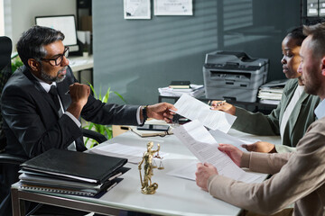 Wall Mural - Young African American businesswoman passing paper document to mature male lawyer during juridical consultation in office