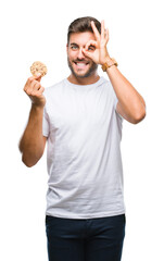 Poster - Young handsome man eating chocolate chips cookie over isolated background with happy face smiling doing ok sign with hand on eye looking through fingers