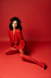 © LIGHTFIELD STUDIOS - A young woman exquisitely dressed in a red suit and tights sitting gracefully on the vibrant studio floor.