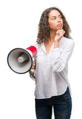 Canvas Print - Young hispanic woman holding megaphone serious face thinking about question, very confused idea