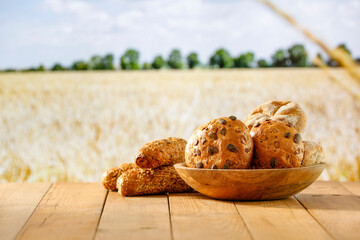 Wall Mural - Fresh baked buns on wooden table top with a blue sky and wheat field background.