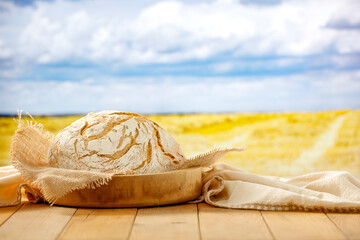 Wall Mural - Loaf of traditional bread and wheat ears on wooden plate on wooden table on a background of wheat field. Copy space for products.