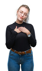 Wall Mural - Young blonde woman wearing glasses over isolated background smiling with hands on chest with closed eyes and grateful gesture on face. Health concept.