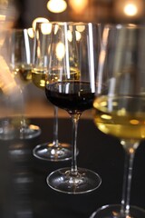 Poster - Different tasty wines in glasses on black table against blurred lights, closeup