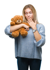 Poster - Young caucasian woman holding cute teddy bear over isolated background cover mouth with hand shocked with shame for mistake, expression of fear, scared in silence, secret concept