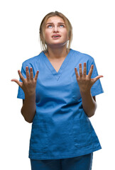 Poster - Young caucasian nurse woman wearing surgeon uniform over isolated background crazy and mad shouting and yelling with aggressive expression and arms raised. Frustration concept.