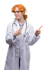 Canvas Print - Young redhead woman wearing doctor uniform smiling and looking at the camera pointing with two hands and fingers to the side.