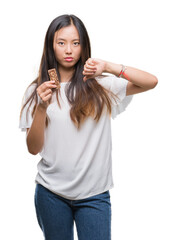 Wall Mural - Young asian woman eating chocolate energetic bar over isolated background with angry face, negative sign showing dislike with thumbs down, rejection concept