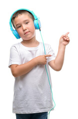 Canvas Print - Dark haired little child listening music with headphones very happy pointing with hand and finger to the side