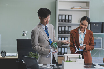 Wall Mural - female alternative energy engineer hold a windmill power sample model and discuss with her male colleague for alternative power in the studio