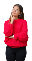 Wall Mural - Young beautiful brunette woman wearing red winter sweater over isolated background with hand on chin thinking about question, pensive expression. Smiling with thoughtful face. Doubt concept.